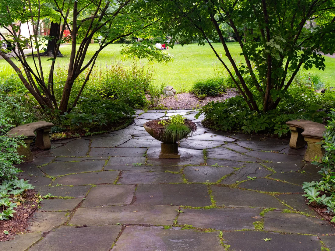 A flagstone terrace under mature trees with a central planter